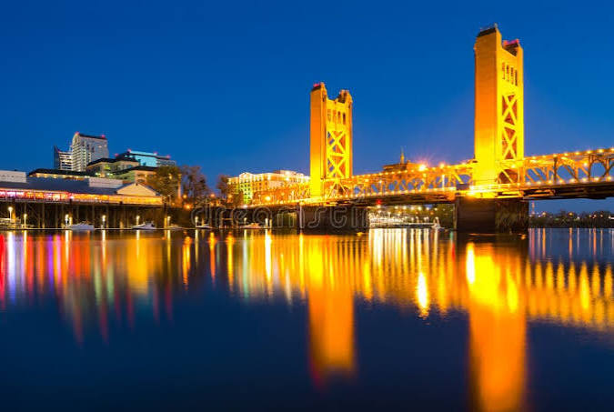 Sacramento Tower Bridge lit gold at night reflecting on the Sacramento River